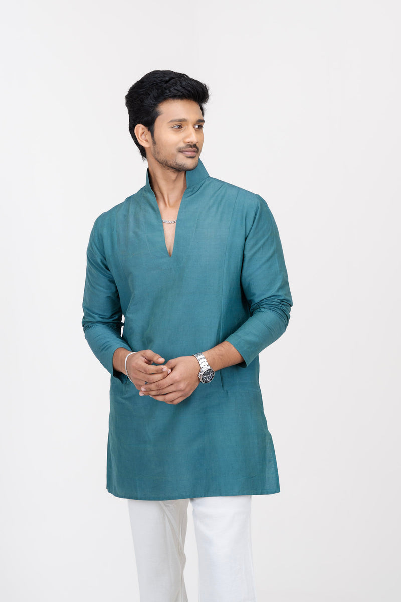 Man in the Mula Aranya dark blue-green kurta and white trousers, hands clasped