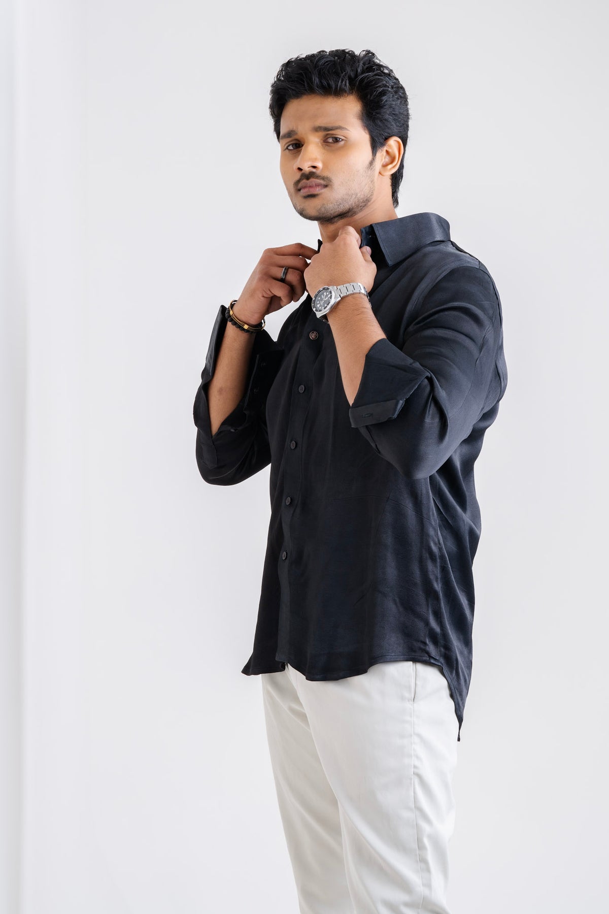 Mula Timir black shirt worn with white trousers, adjusting the collar